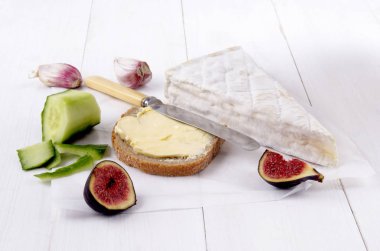 Fransız peyniri, tereyağı, incir, sarımsak, bıçak ve soyulmuş salatalık ile ekmek beyaz kağıt üzerine dilim