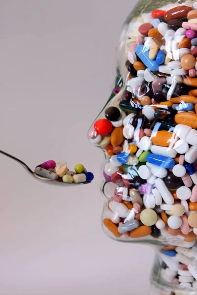 stock image glass bottle in form of human face with colorful medicine pills and spoon,  close-up  