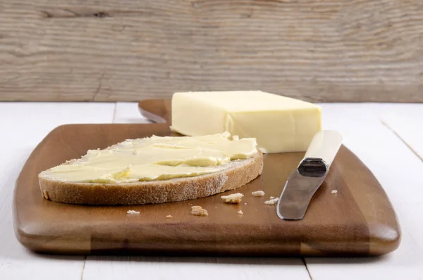 用黄油和小刀在木板上切面包片 — 图库照片