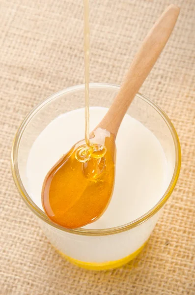 ガラスと木のスプーンの上に有機蜂蜜ホットミルク — ストック写真