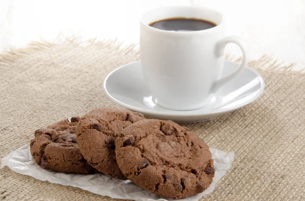 Chocolate Biscuit On White Paper And A Cup Of Coffee In The Background