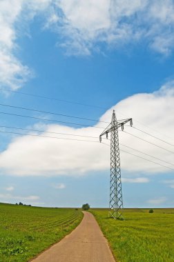 Yüksek gerilim iletim kule mavi gökyüzü arka plan üzerinde road yakınındaki çayır 