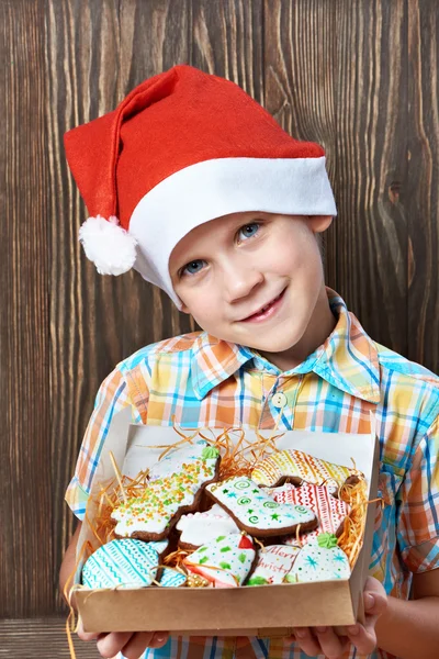 Μικρό αγόρι στο Πρωτοχρονιάτικο κόκκινο καπάκι με κουτί μπισκότα Χριστουγέννων — Φωτογραφία Αρχείου