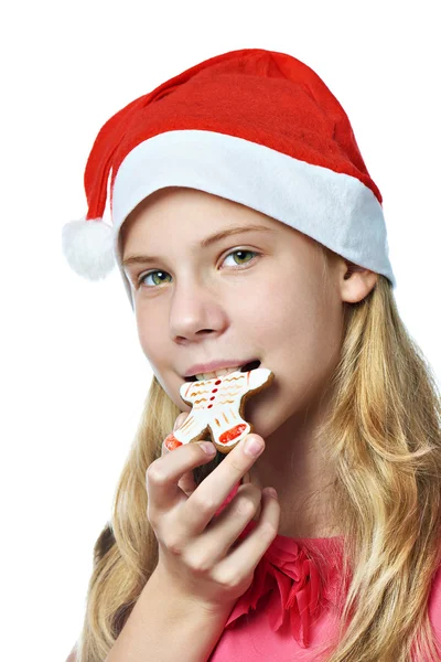 Happy teen girl in red cap eating Christmas cookie isolated — Stock Photo, Image