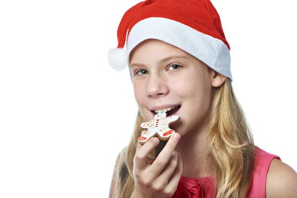 Happy teen girl in red cap eating Christmas cookie isolated — Stock Photo, Image