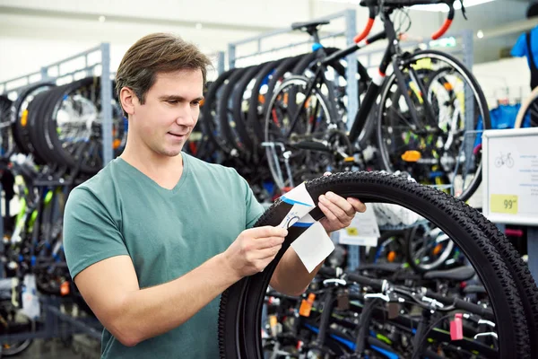 Hombre elige neumático para andar en bicicleta en tienda de deportes — Foto de Stock