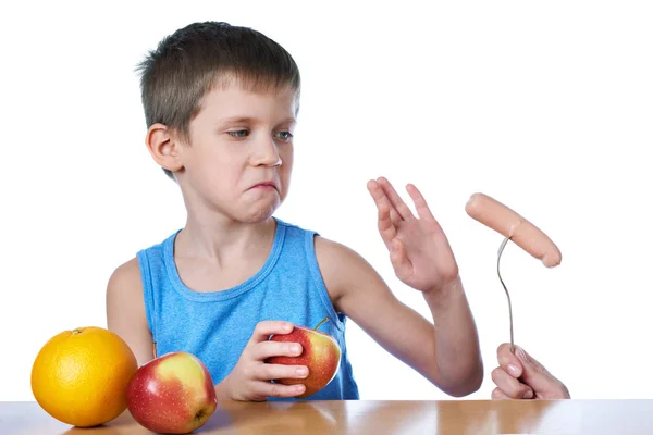 Boy with apples and orange against harmful sausage — Stock Photo, Image
