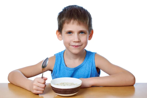 Menino feliz comendo mingau na mesa isolado — Fotografia de Stock