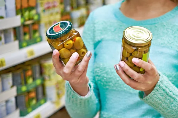 Mulher escolhe azeitonas enlatadas no supermercado — Fotografia de Stock