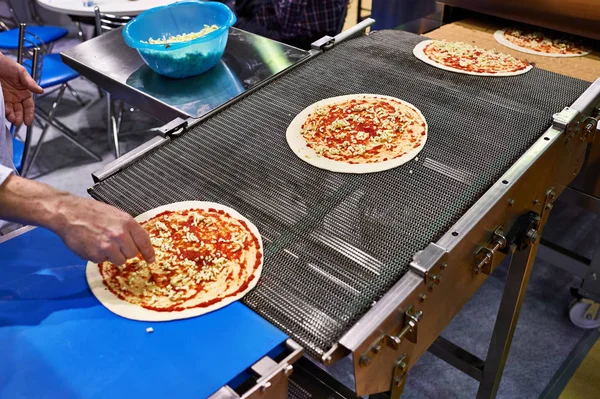 Cocinero trabajador añade queso a la pizza en el transportador — Foto de Stock