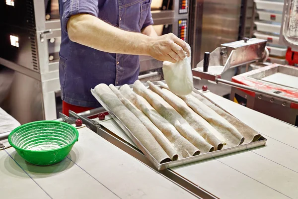 Baker pours flour on bread loaves before baking — Stock Photo, Image