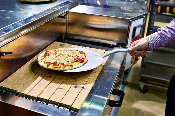 Prepared pizza on metal spatula is taken from conveyor — Stock Photo, Image