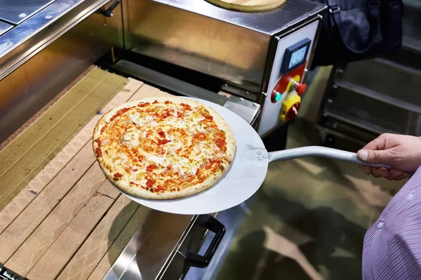 La pizza preparada en la espátula metálica se toma del transportador — Foto de Stock