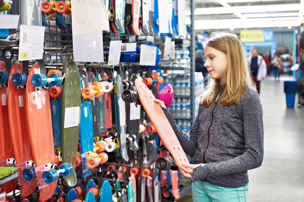 Adolescente chica elige monopatín en tienda de deporte —  Fotos de Stock