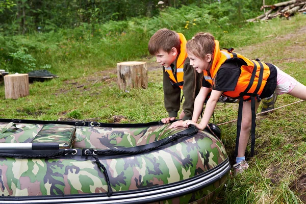 Children in life jackets push boat into water — Stock Photo, Image