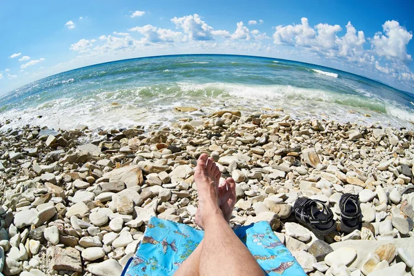 Voeten van man rust en zonnebaden op de rotsachtige strand — Stockfoto