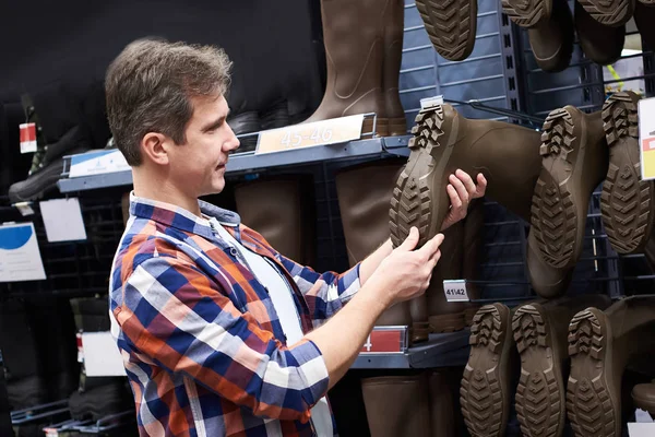 Man kiest rubber laarzen voor de jacht en de visvangst in de winkel — Stockfoto