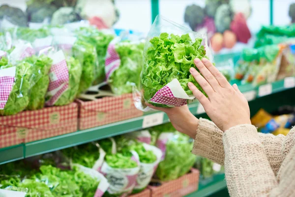 Mujer elige ensalada de hojas verdes en la tienda de comestibles — Foto de Stock