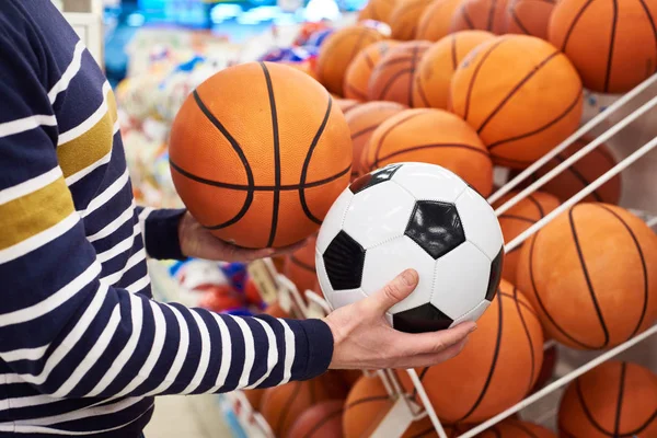 Comprador manos con el fútbol y el baloncesto en la tienda de deportes —  Fotos de Stock