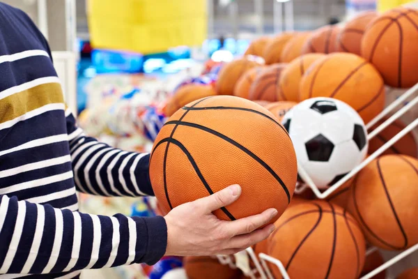 Руки покупателя с футболом и баскетболом в спортмагазине — стоковое фото