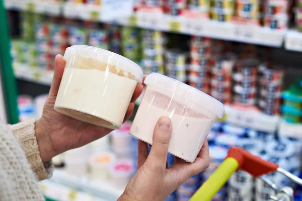 Руки покупателя с пластиковыми банками йогурта в продуктовом магазине — стоковое фото