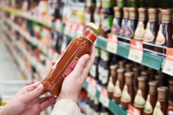 Koper handen met fles saus in winkel — Stockfoto