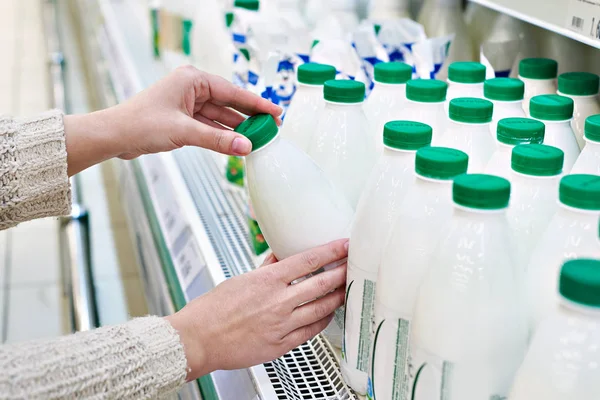 Woman takes bottle of milk from shelf in grocery — Stock Photo, Image