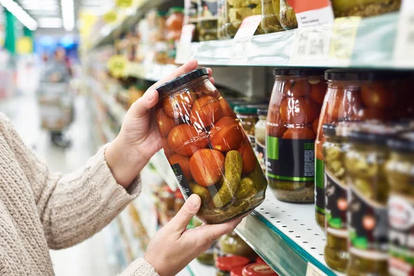 Handen met blikje gezouten tomaten en komkommers in de winkel — Stockfoto