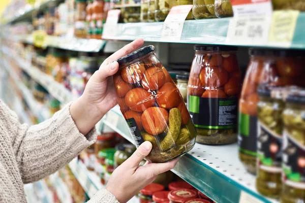 Händer med kan saltade tomater och gurkor i butik — Stockfoto