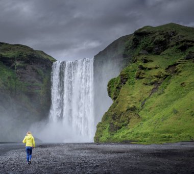 Yaz, İzlanda 'da Skogafoss şelalesinin yanında yürüyen genç bir kız.