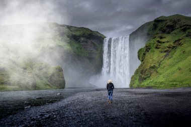 Yaz, İzlanda 'da Skogafoss şelalesinin yanında yürüyen genç bir kız.