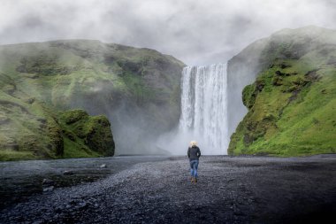 Yaz, İzlanda 'da Skogafoss şelalesinin yanında yürüyen genç bir kız.