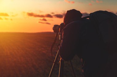 Üç ayaklı ve kameralı fotoğrafçı gün batımında geniş bir alanda manzara çeker.