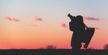 Üç ayaklı ve kameralı fotoğrafçı gün batımında geniş bir alanda manzara çeker.