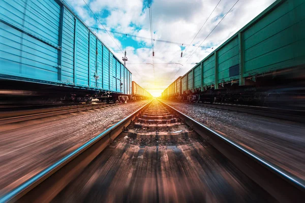 Yük trenleri, kırmızı ve mavi, sarı güneş ve gökyüzünün arka planına karşı demiryolu üzerinde dururlar.