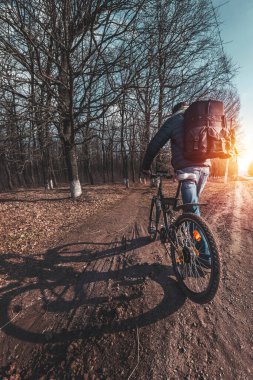 Büyük bir sırt çantası ve elinde bisiklet olan bir adam ormanda bir patika boyunca yürüyor.