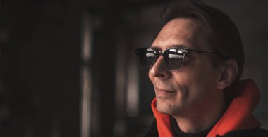 Güneş gözlüklü adam başka tarafa bakıyor, karanlık bir arka plana yakından bakıyor.