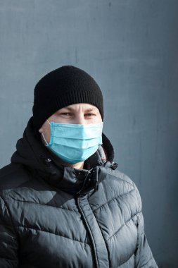 Şehrin gri arka planında mavi koruyucu tıbbi maskeli bir adam var.