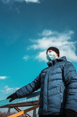 Şehirdeki mavi koruyucu tıbbi maskeli adam köprü ve gökyüzünün arka planına karşı