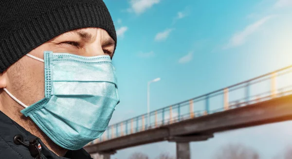 Şehirdeki mavi koruyucu tıbbi maskeli adam köprü ve gökyüzünün arka planına karşı