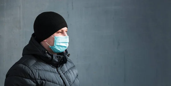 Şehrin gri arka planında mavi koruyucu tıbbi maskeli bir adam var.