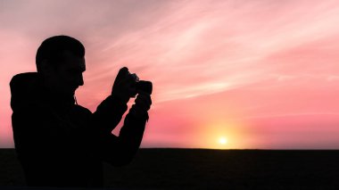 Gün batımında eski bir mekanik kamerayla fotoğraf çeken bir adamın silueti.