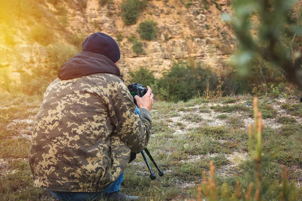 Kamuflaj ceketli bir fotoğrafçı bir dağın fotoğrafını çekiyor.