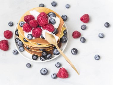 lezzetli taze yaban mersini ve ahududu plaka beyaz masada tahta kaşıkla, kopya alanı ile üstten görünüm ile krep yığını