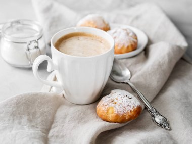 Kek profiterol bardak latte ile beyaz tabakta pudra şekeri serpilir
