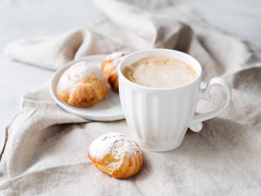 Kek profiterol bardak latte ile beyaz tabakta pudra şekeri serpilir