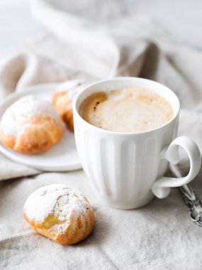 Kek profiterol bardak latte ile beyaz tabakta pudra şekeri serpilir