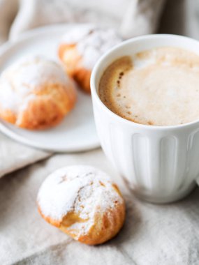 Kek profiterol bardak latte ile beyaz tabakta pudra şekeri serpilir