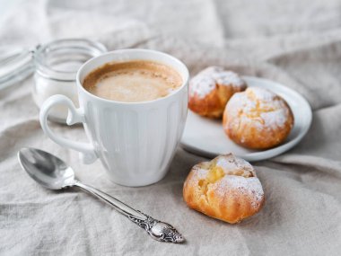 Kek profiterol bardak latte ile beyaz tabakta pudra şekeri serpilir