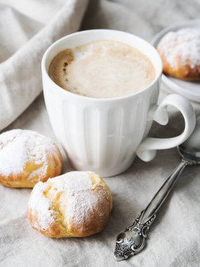 Kek profiterol bardak latte ile beyaz tabakta pudra şekeri serpilir